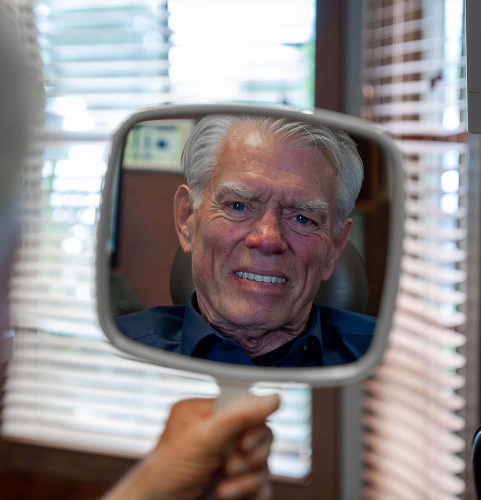 Patient smiling into mirror after full mouth implants